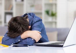 a boy in need of sleep disorder treatment naps near a computer