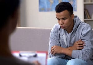 a teen boy thinks while a therapist takes notes during somatic therapy